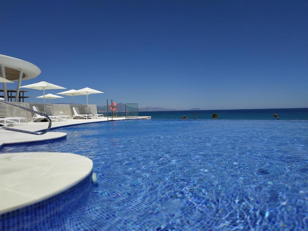 uma piscina com cadeiras e guarda-sóis numa praia em Apartamento SIDI Resort de lujo en Playa San Juan em Alicante