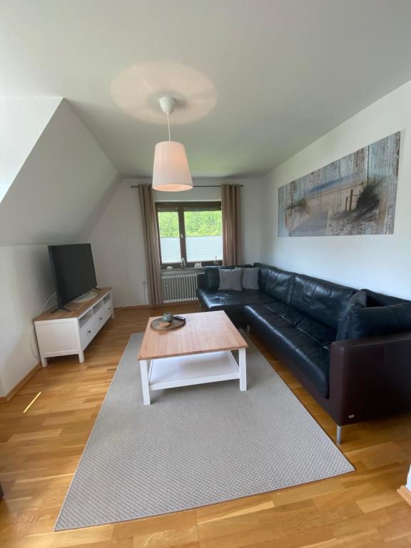 a living room with a black leather couch and a coffee table at Gemütliche Ferienwohnung Nesco mit eingezäunten Garten in Aurich