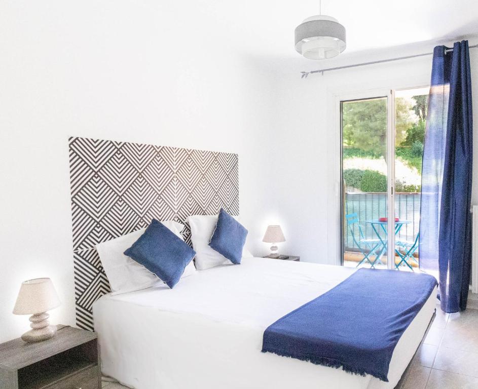 a white bedroom with a large bed with blue pillows at Les Mimosas in Roquebrune-Cap-Martin