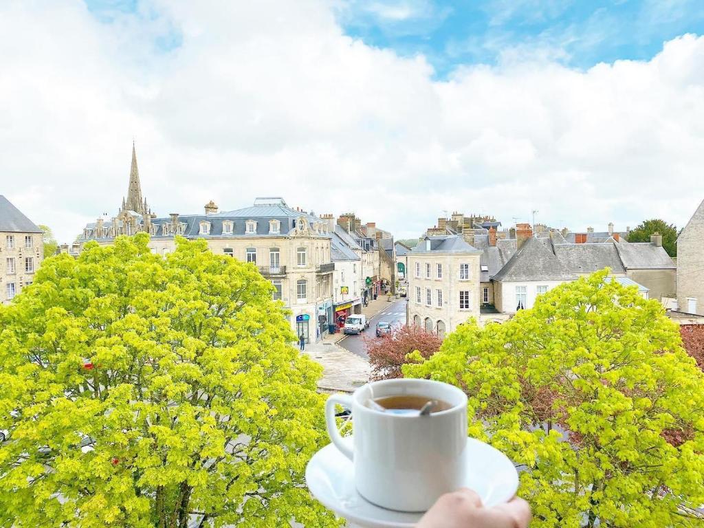 una persona sosteniendo una taza de café en un balcón en Hôtel Le Vauban, en Carentan