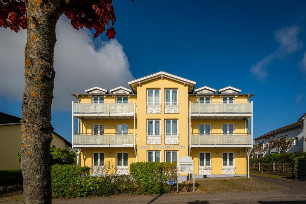 un bâtiment jaune avec des balcons blancs et un arbre dans l'établissement Haus Sonnenschein Göhren, à Göhren