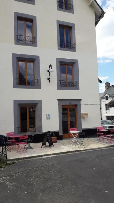 un bâtiment blanc avec des tables et des chaises devant lui dans l'établissement La Maison en Cézallier - Purple, à Marcenat