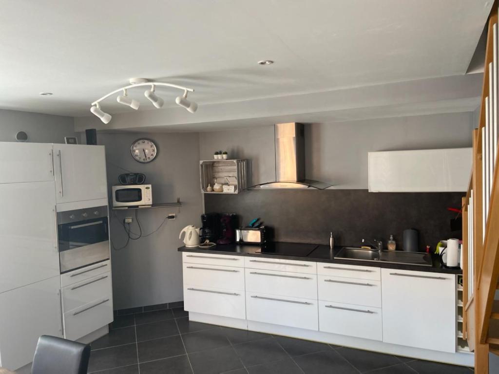 a kitchen with white cabinets and a clock on the wall at le gite d'olhain in Fresnicourt-le-Dolmen