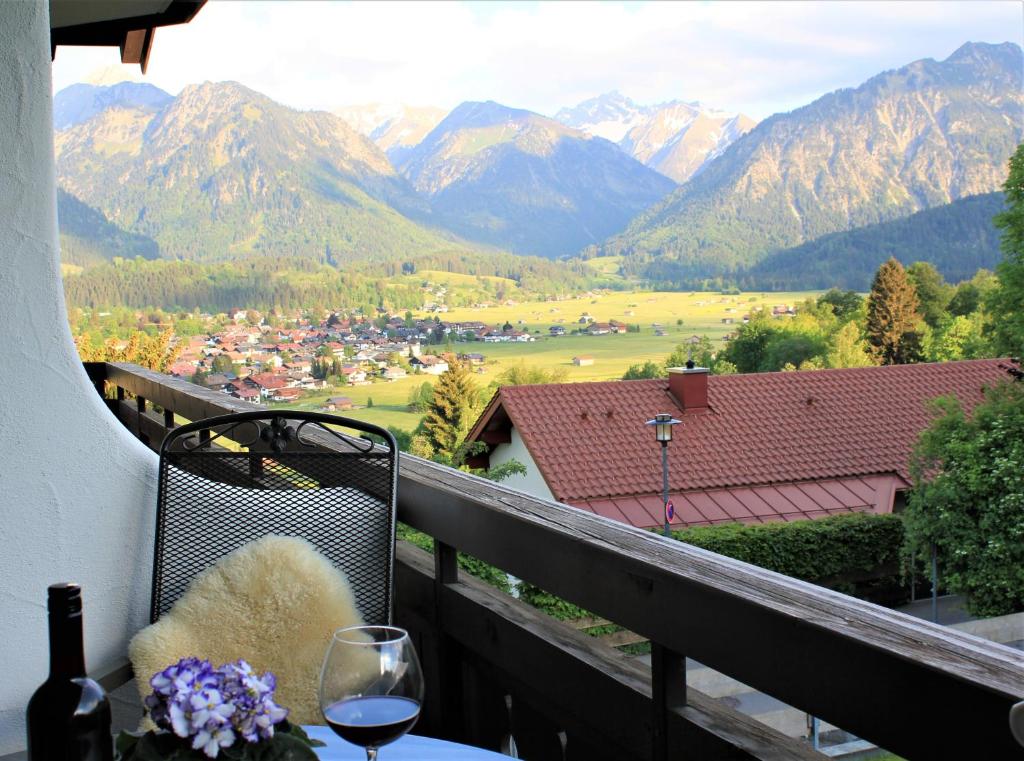 a table with a glass of wine on a balcony with mountains at Ferienwohnung Bergflora in Oberstdorf