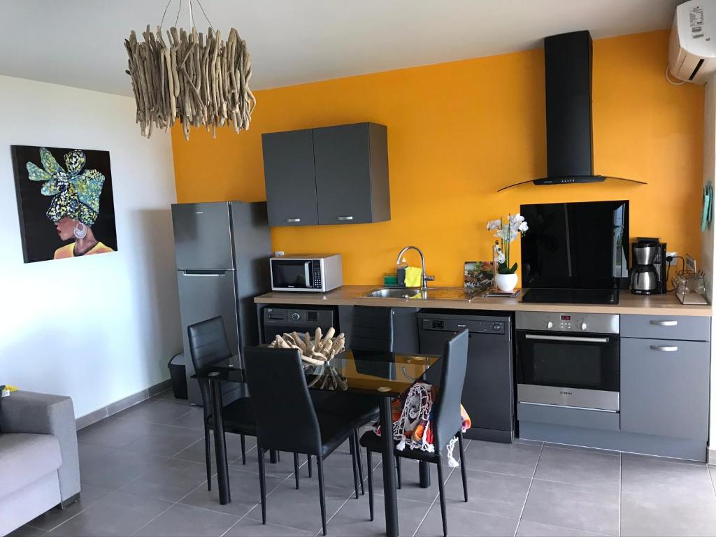 a kitchen with a dining table and a kitchen with yellow walls at Gîte Maracudja vue sur mer in Capesterre-Belle-Eau