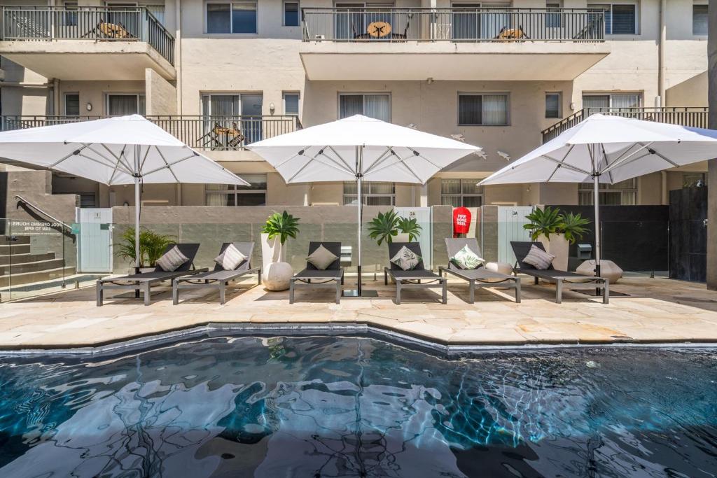 a swimming pool with umbrellas and chairs and a building at Byron Bay Hotel and Apartments in Byron Bay