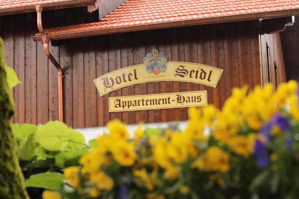ein Schild vor einem Gebäude mit gelben Blumen in der Unterkunft Hotel Seidl in Straßlach-Dingharting
