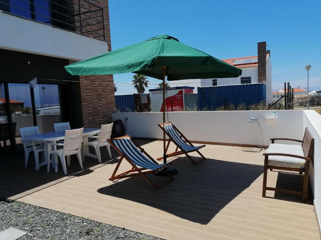 um pátio com um guarda-sol verde, cadeiras e uma mesa em Casa da Praia em Porto Côvo em Porto Covo