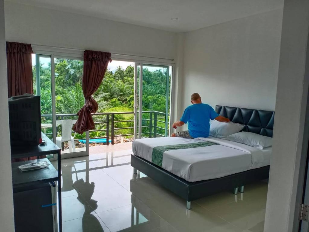 a man sitting on a bed in a bedroom at Tom's house in Khura Buri