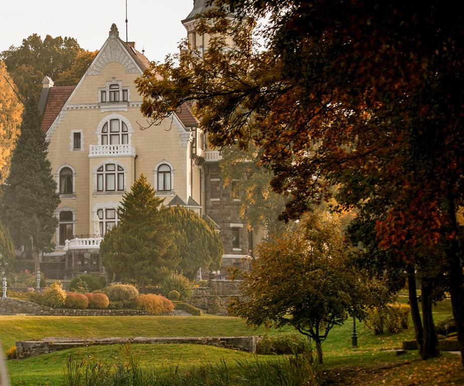 una gran casa blanca con un árbol delante en Hotel Bursztynowy Pałac, en Koszalin