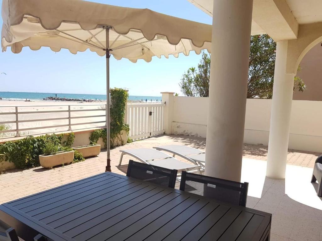 a porch with a table and an umbrella and the beach at Belle villa sur vaste plage Palavas Montpellier in Palavas-les-Flots