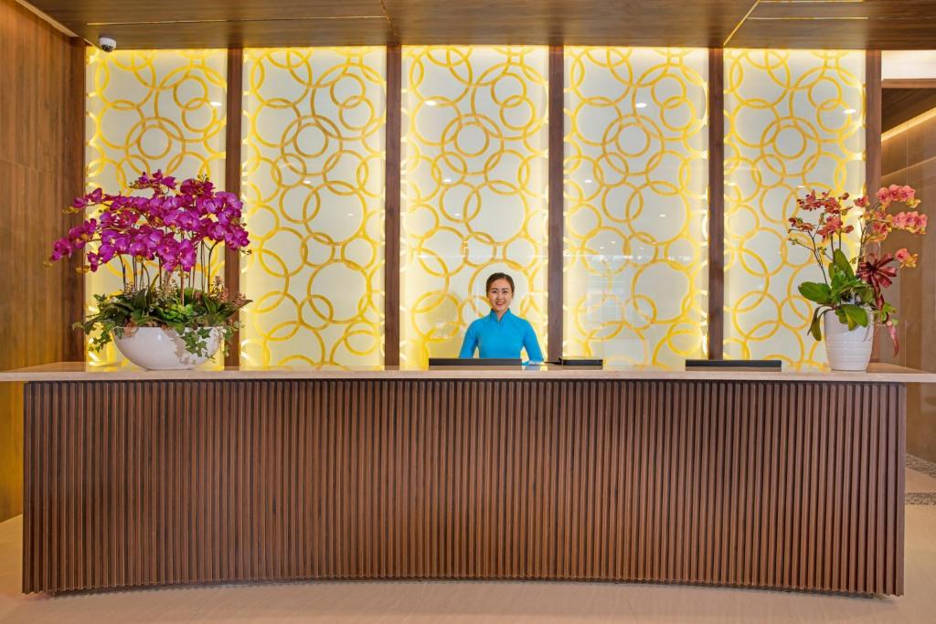 A warmly lit reception desk is framed by orchids and patterned panels.