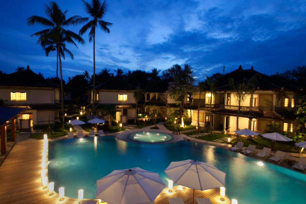 uma vista para uma piscina à noite com guarda-sóis em Grand Whiz Hotel Nusa Dua Bali em Nusa Dua