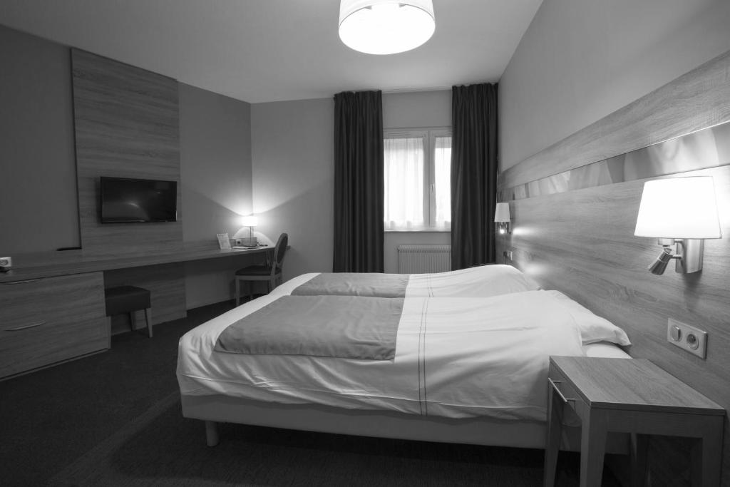 a bedroom with a bed and a desk and a television at Hotel Restaurant Le Coquelicot in Burnhaupt-le-Haut