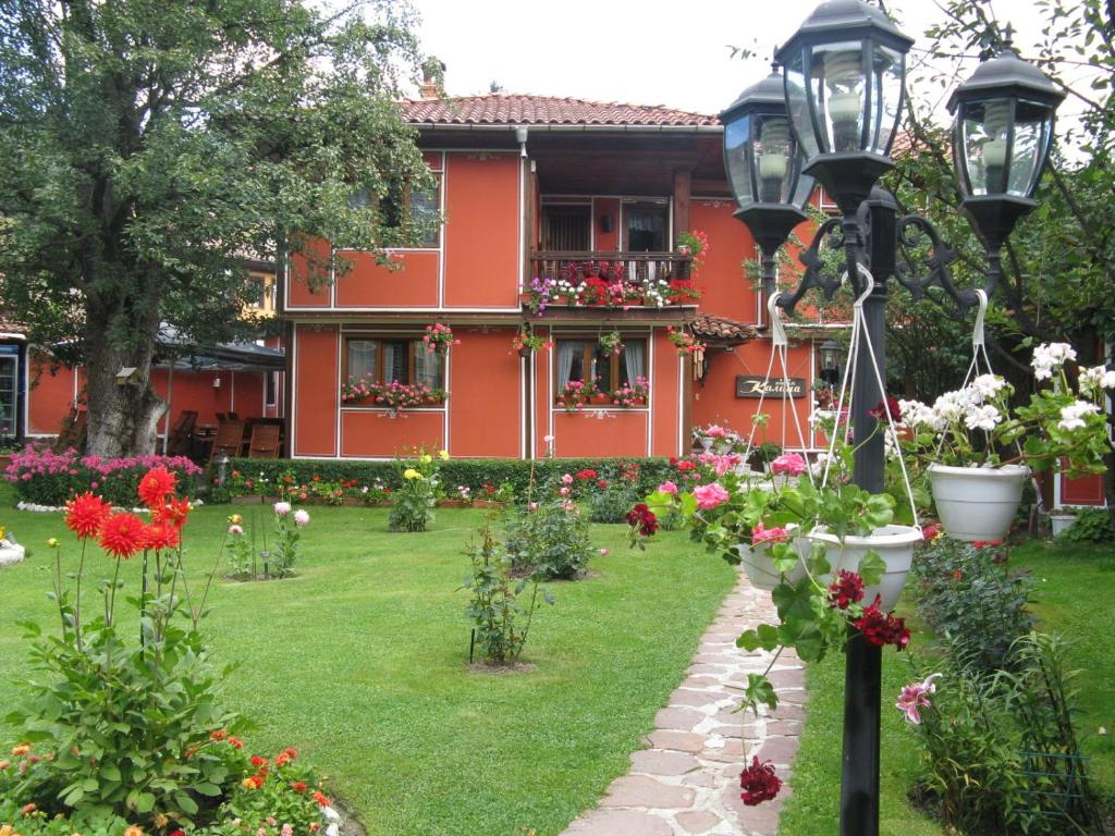 a garden in front of a red house with flowers at Family Hotel Kalina in Koprivshtitsa