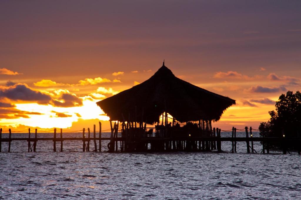 a hut on the water with a sunset in the background at Fundu Lagoon in Pemba