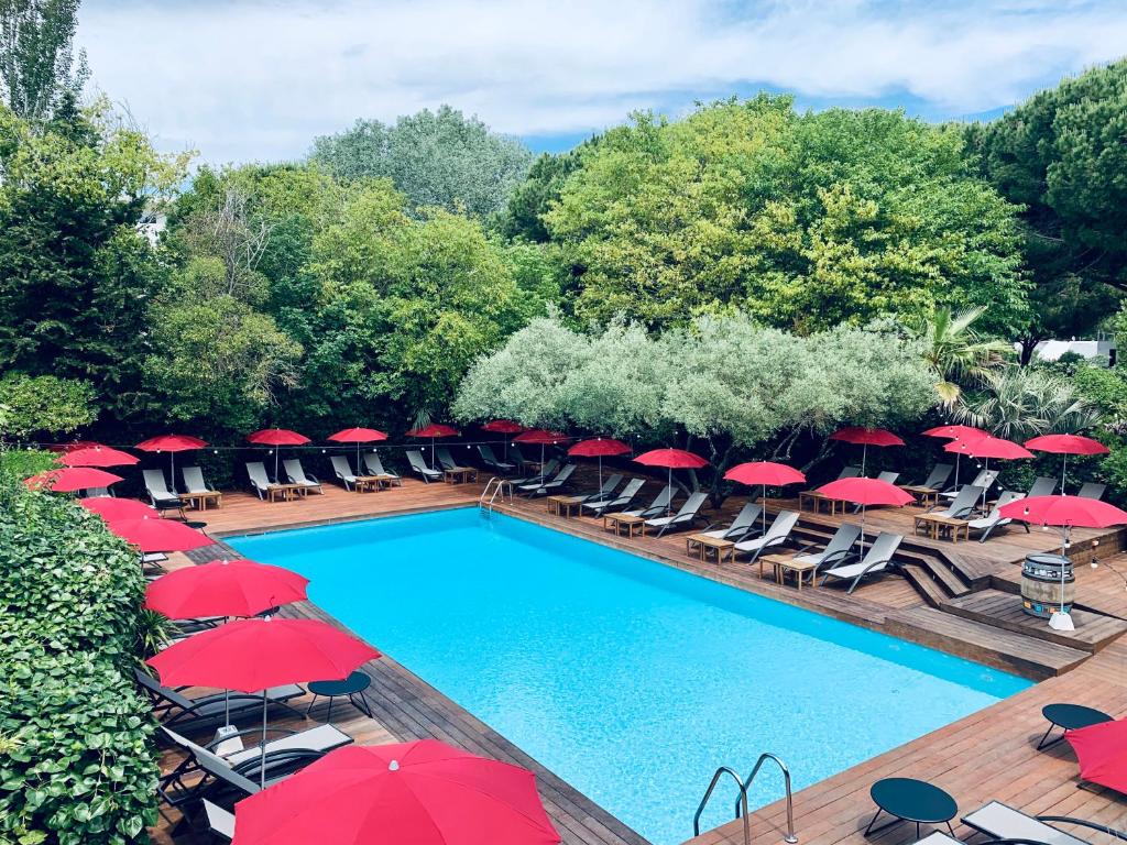 a swimming pool with red umbrellas and lounge chairs at Le Prose Hôtel in La Grande Motte