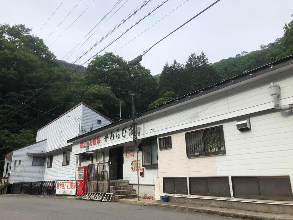 ein weißes Gebäude mit einer roten Tür auf einer Straße in der Unterkunft Minshuku Kawarabi-so in Nosegawa