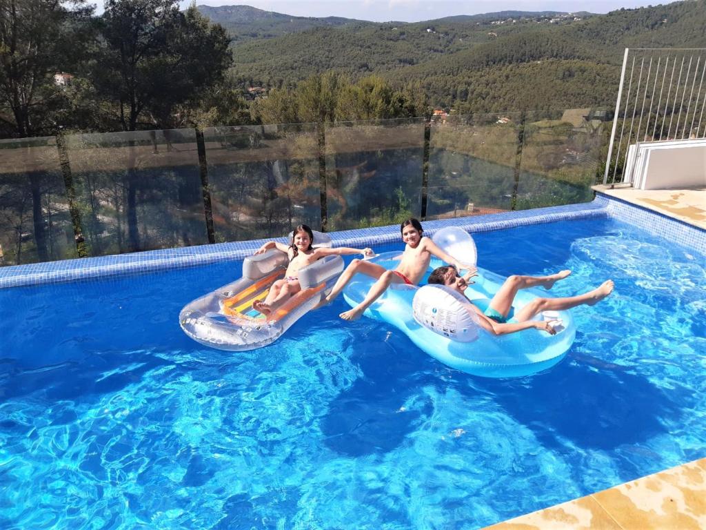 Drei Personen fahren auf aufblasbaren Gegenständen in einem Schwimmbecken in der Unterkunft Villa Mur - Espectacular villa cerca de Sitges y BCN in Olivella