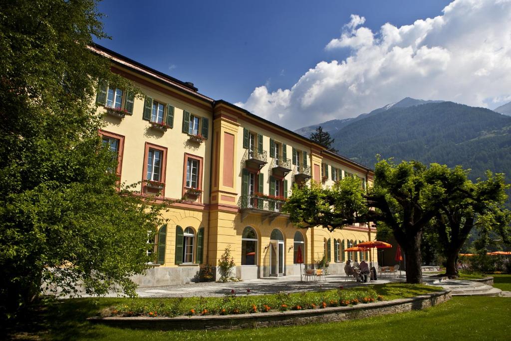 a large yellow building with mountains in the background at Hotel Le Prese in Poschiavo