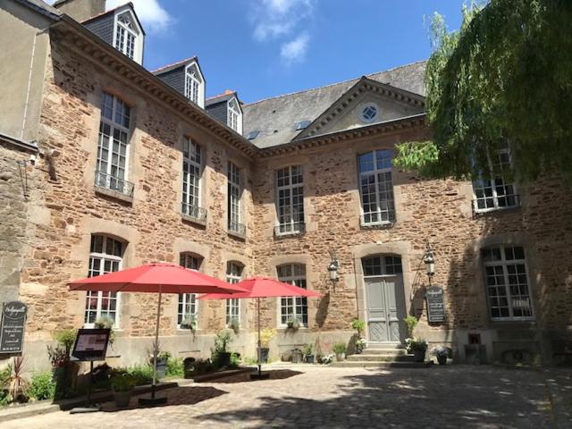 un grand bâtiment en briques avec des parapluies rouges devant lui dans l'établissement Perlépampille, à Dinan