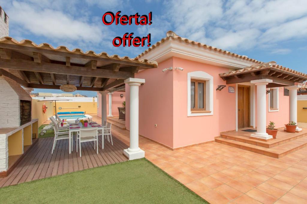ein rosafarbenes Haus mit einem Tisch und Stühlen auf einer Terrasse in der Unterkunft Villa Bella Lucia 1. Piscina Climatizada, WiFi, BBQ. in Corralejo