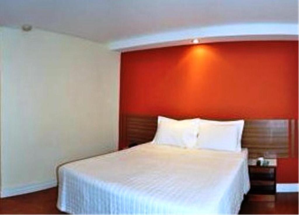 a bedroom with a white bed with an orange headboard at Hotel Vollare in Osasco