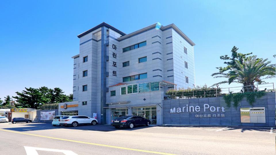 ein weißes Gebäude mit Autos auf einem Parkplatz in der Unterkunft Marine Port Resort in Seogwipo
