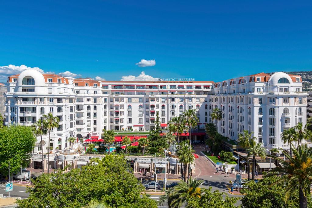 un grand bâtiment blanc avec des palmiers devant lui dans l'établissement Hôtel Barrière Le Majestic Cannes, à Cannes