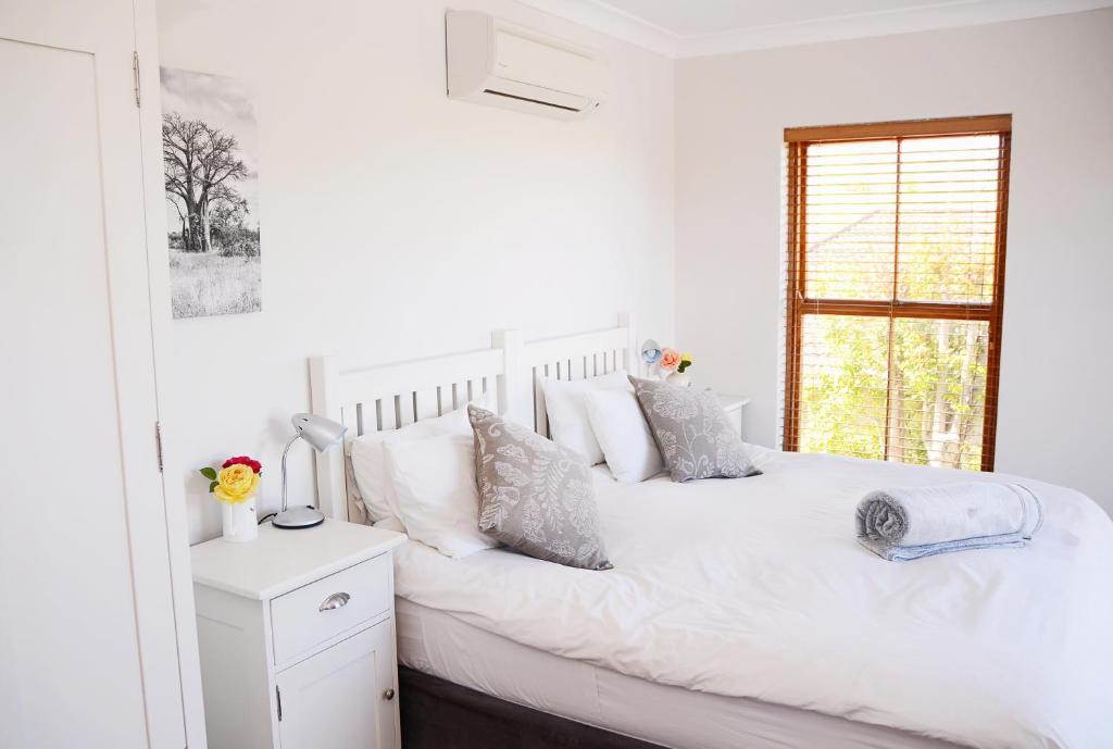 a white bedroom with a white bed and a window at Penelope's Stellenbosch in Stellenbosch