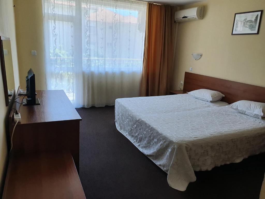 a bedroom with a bed and a desk and a window at Sandor Hotel in Nesebar