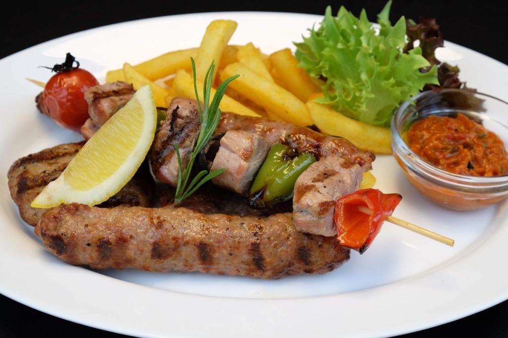 a white plate of food with meat and french fries at Lotus Family Hotel - Free Parking in Sunny Beach
