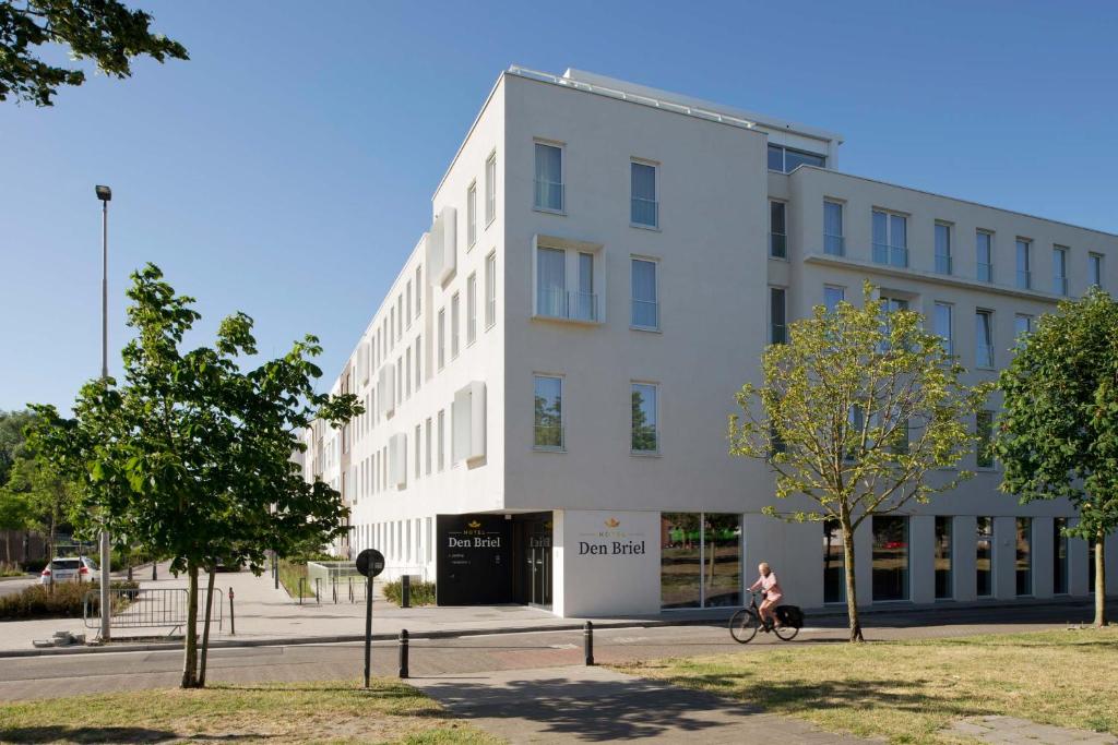 une femme faisant du vélo devant un bâtiment blanc dans l'établissement Hotel Den Briel, à Gand