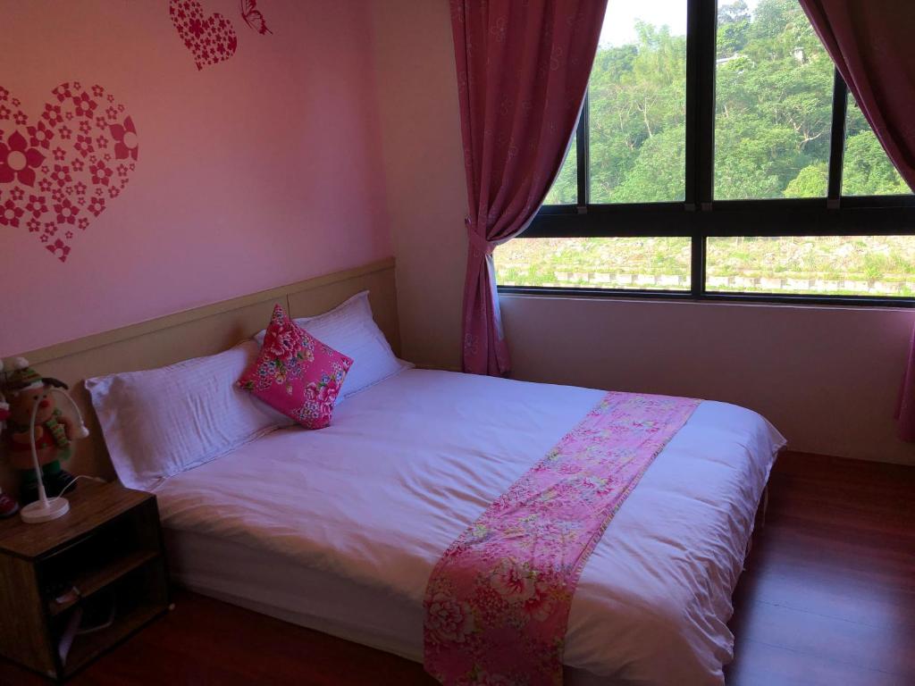 a bedroom with a white bed with pink pillows and a window at 甘丹民宿-三義火車站前 in Sanyi
