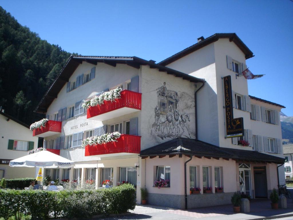 un gran edificio blanco con balcones rojos y una sombrilla en Hotel Posta en Le Prese, Poschiavo