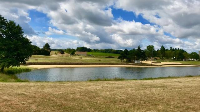 een vijver in een veld met een bewolkte hemel bij Gite Le Bois aux Moines in Lavaré