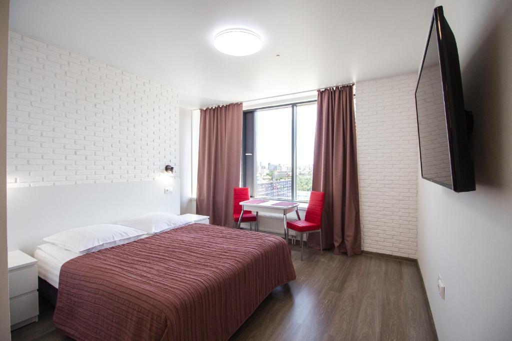 エカテリンブルクにあるAllen Park in Radiusのベッド、テーブル、赤い椅子が備わるホテルルームです。