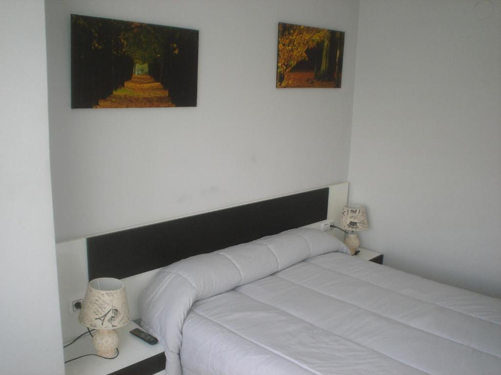 uma cama branca num quarto com duas fotografias na parede em HOSTAL CID em Ourense