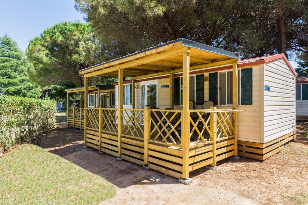 une petite maison avec une grande terrasse couverte dans une cour dans l'établissement Camping Adria Mobile Homes in Brioni Sunny Camping, à Pula