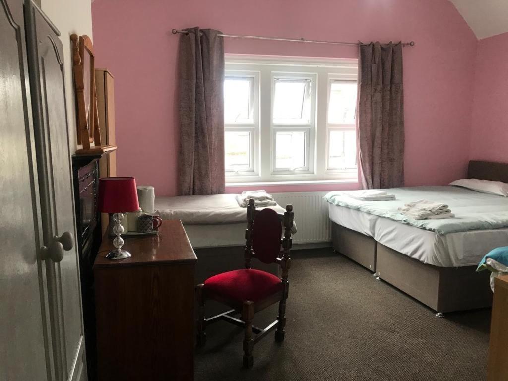 a bedroom with two beds and a desk and a window at Heathrow Stay in Hounslow