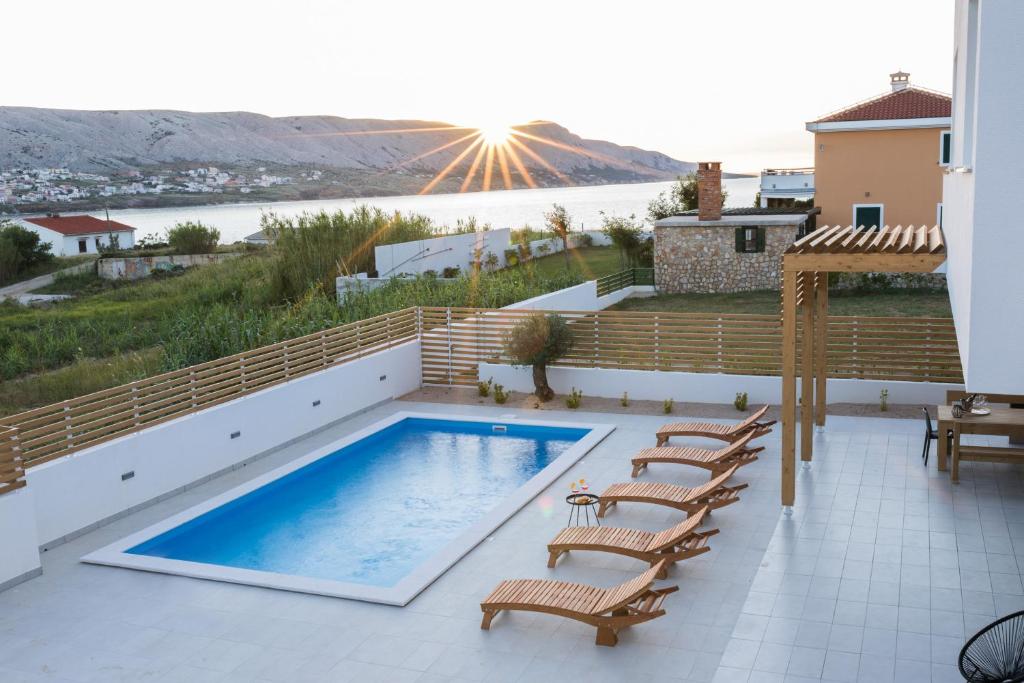 a patio with a swimming pool and chairs and the sun at Villa Belveder in Pag