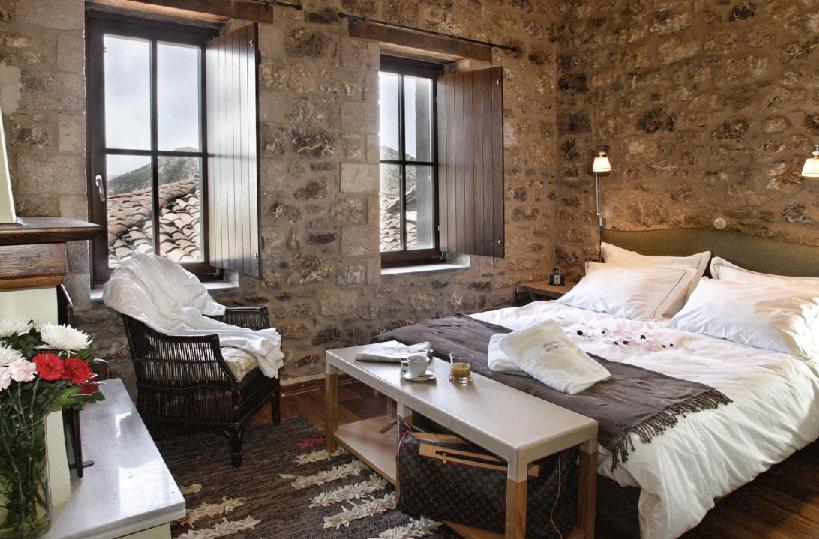 a bedroom with a bed and a table and windows at Guesthouse Theonimfi in Dimitsana