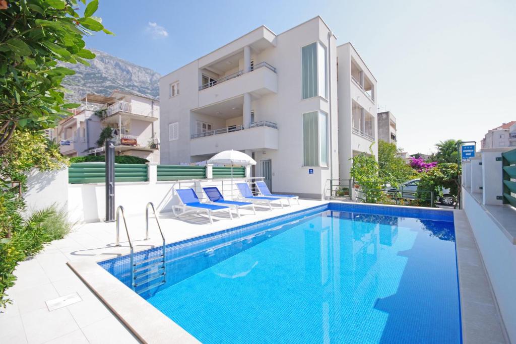 a swimming pool with chairs next to a building at Apartmani Srzic in Makarska