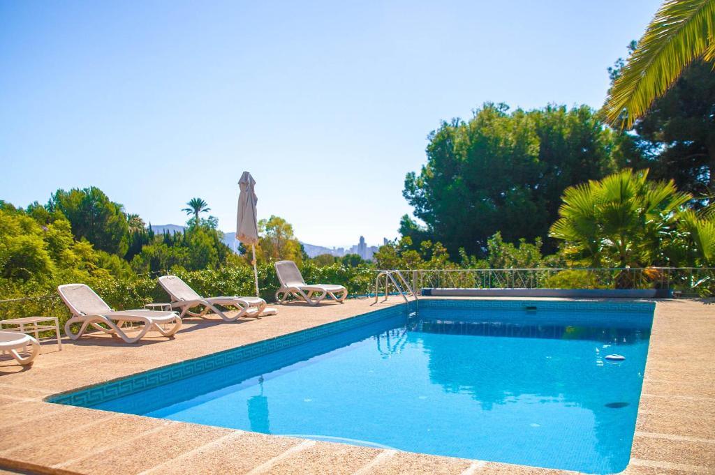 een zwembad met 2 stoelen en een parasol bij Villa Altozano with pool, barbeque, large garden, and fantastic sea views in Benidorm
