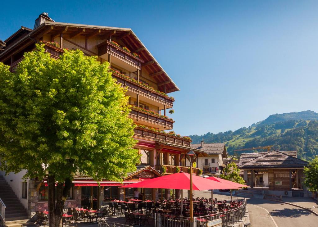 a building with tables and umbrellas in front of it at Logis La Croix-Saint-Maurice in Le Grand-Bornand