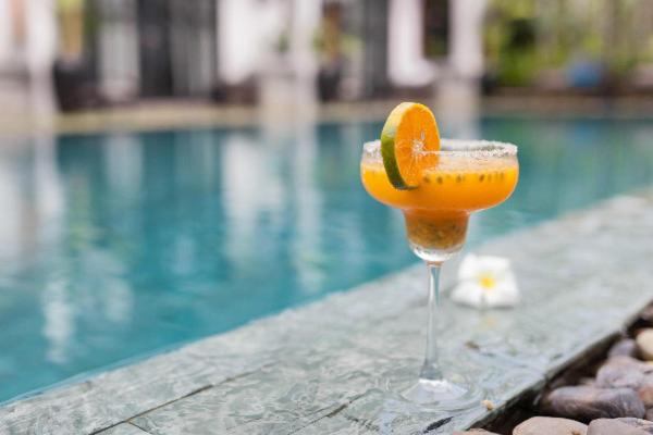 a glass of orange juice sitting next to a swimming pool at The Bali Bubble in Sanur