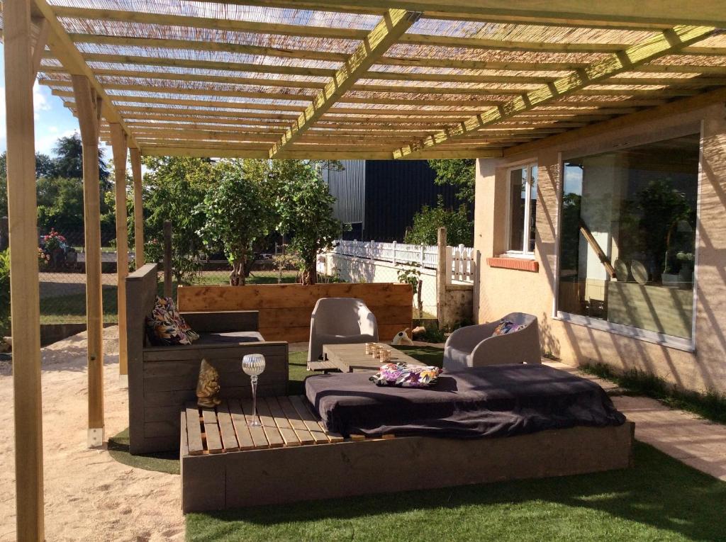 un patio con una cama y sillas bajo una pérgola de madera en La Mardelle, en Saint-Gervais-la-Forêt