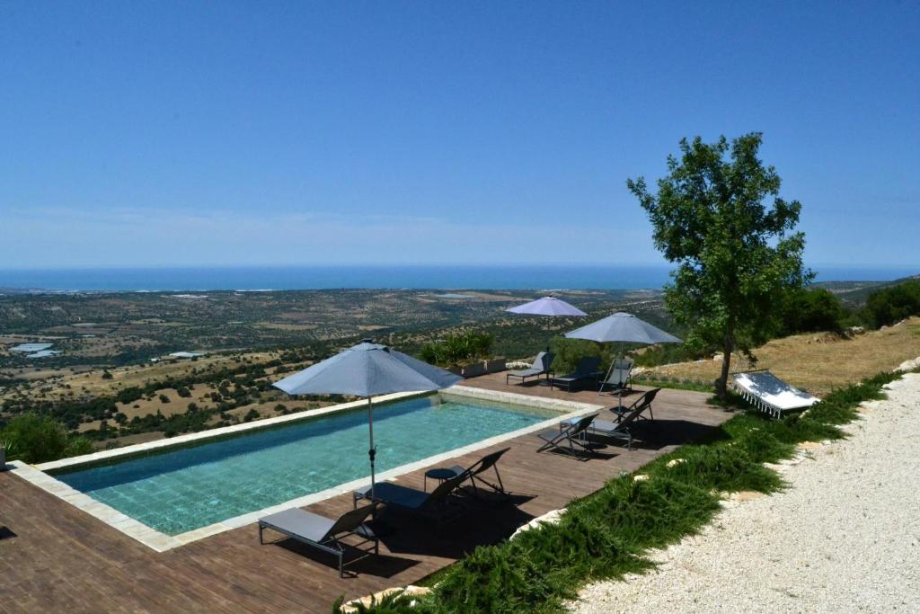 a swimming pool with chairs and umbrellas on a hill at Madre in Ragusa