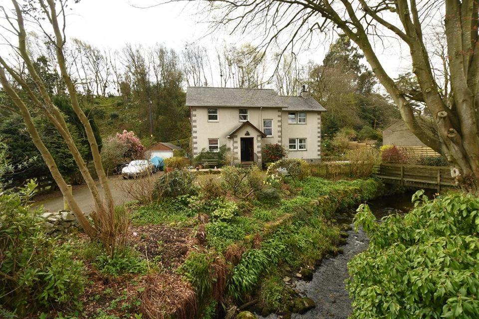 una casa en medio de un jardín con un arroyo en Grovewood House Retreat en Kirkbean