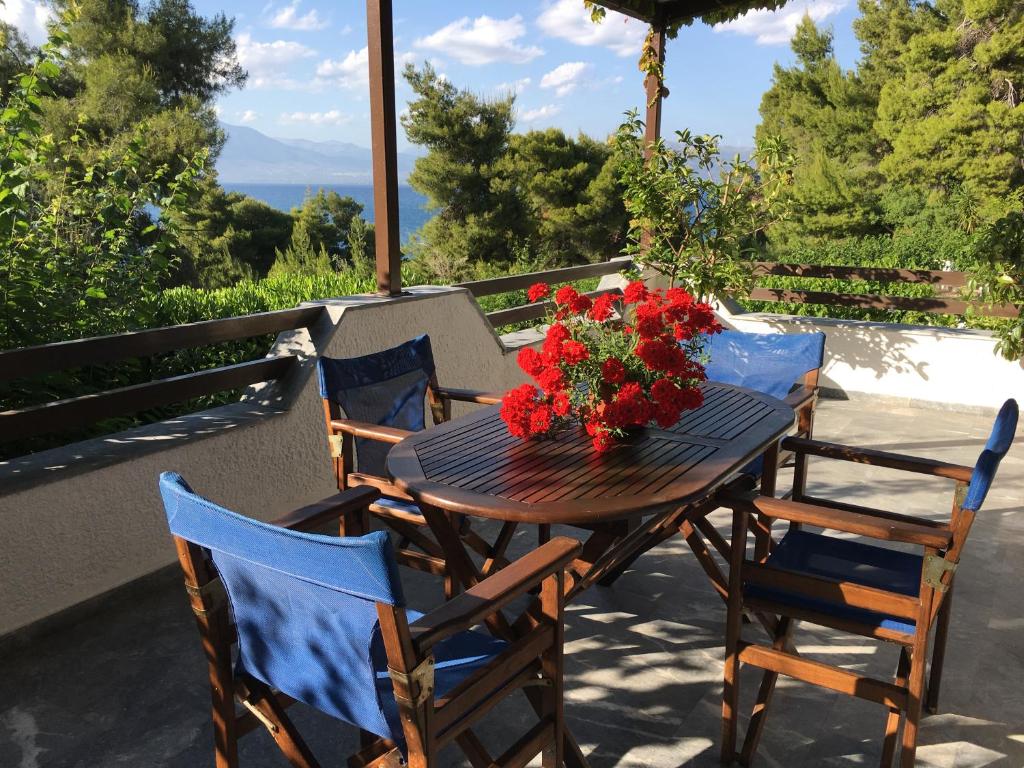 a wooden table and chairs with a bouquet of red flowers at ILIOCHARI sea view apartments Oropos - Kalamos in Kalamos